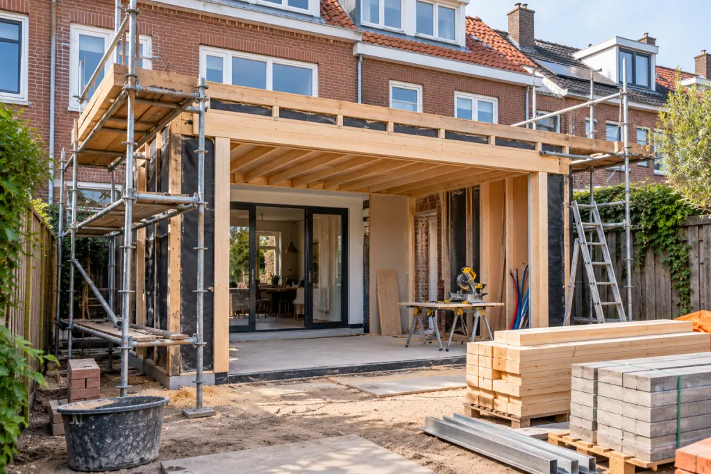 Aanbouw in aanbouw aan de achterkant van een bakstenen woning, met steigers en bouwmateriaal
